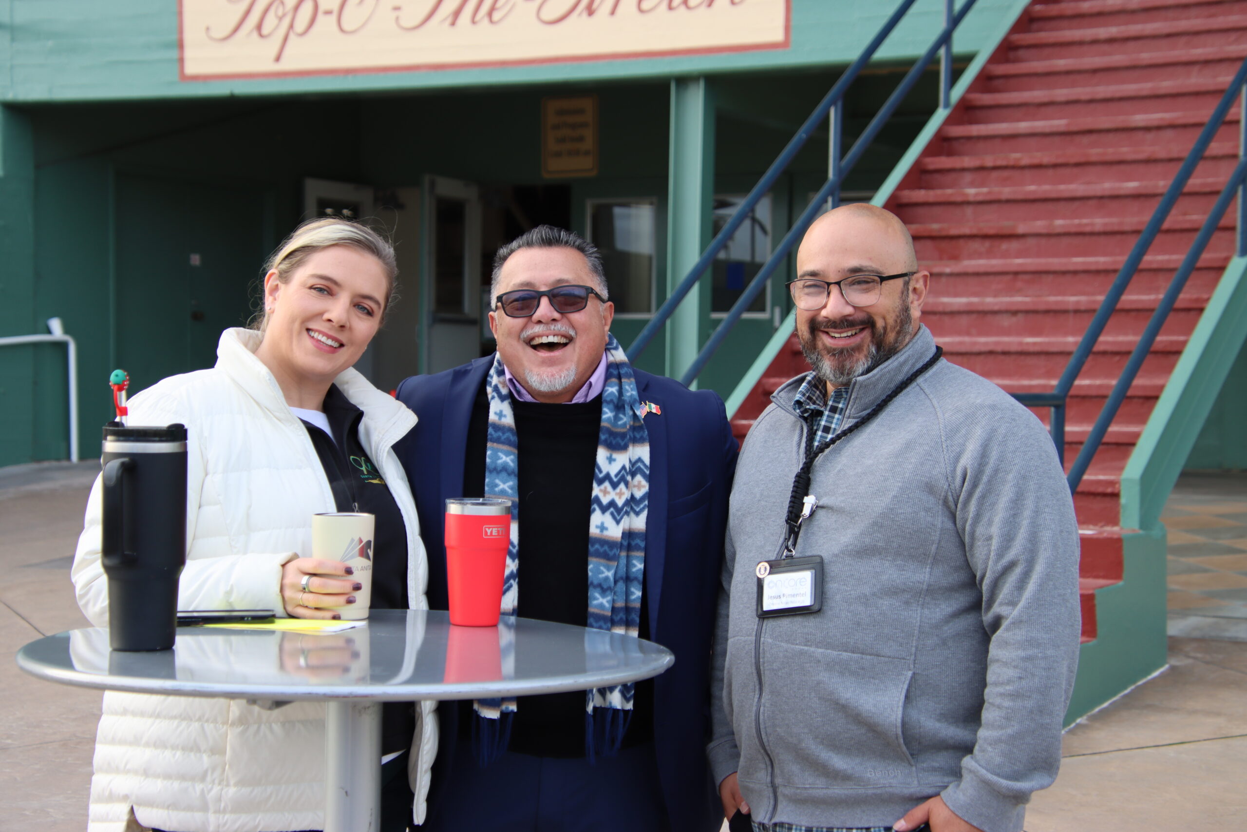 IMG_9750 a woman and two men standing at a tall table with coffee cups in front of them