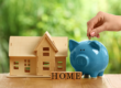 a blue piggy bank sitting next to a small wooden house and a sign with the word home on it