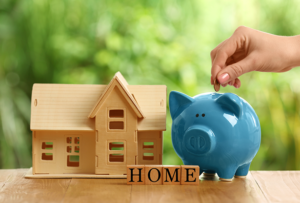 a blue piggy bank sitting next to a small wooden house and a sign with the word home on it