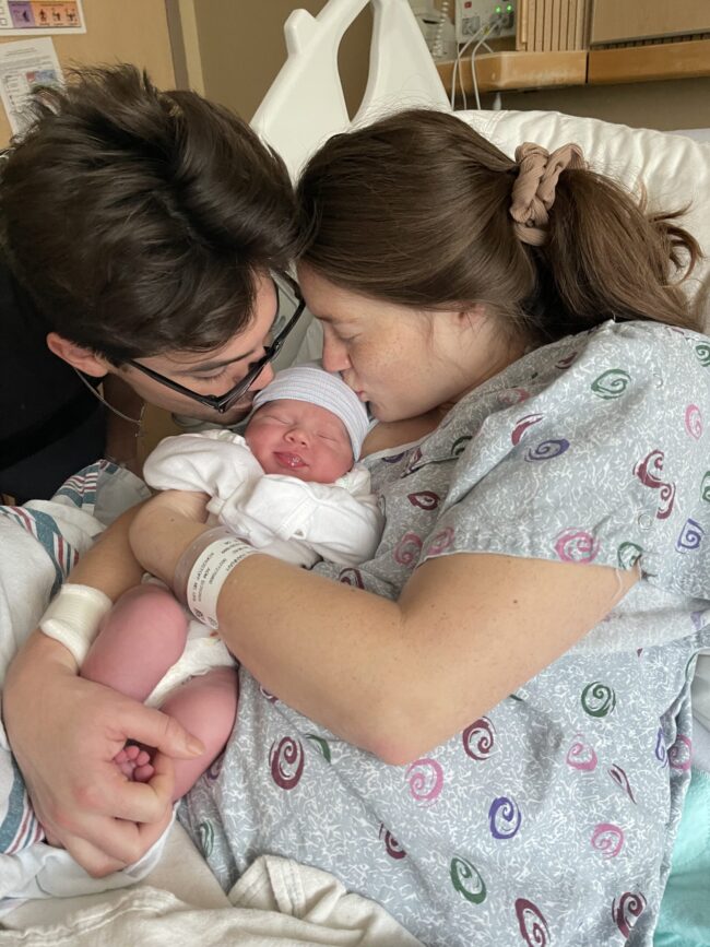 two parents kissing their newborn baby