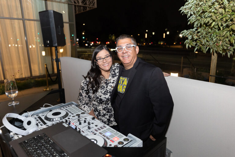a woman in a patterned dress with a man in a black suit and white glasses
