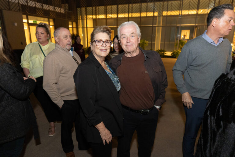 a woman in a black sweater with her arm around a man in a brown shirt and black jacket