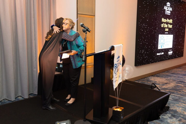 two women exchanging a hug on a stage beside a podium