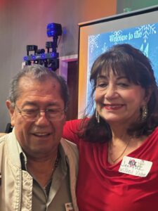 a woman in red standing with a man wearing glasses and a tan shirt 
