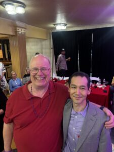 a man in a red shirt standing with his arm around a shorter man in a gray suit jacket