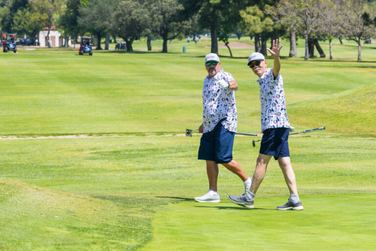 two men in matching golf outfits waving and giving thumbs up to the camera