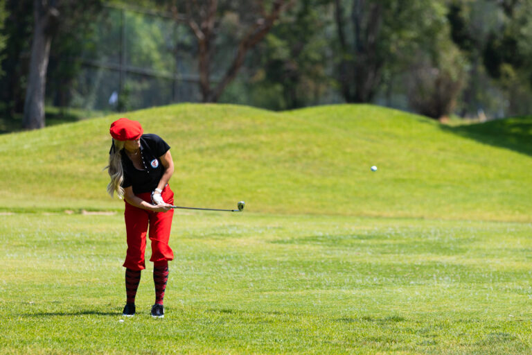 a woman in a black shirt with red golf pants and hat putts a ball on a golf course
