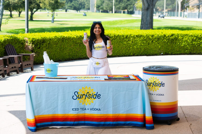 a woman in a white dress standing behind a table set with a Surfside Vodka table cloth