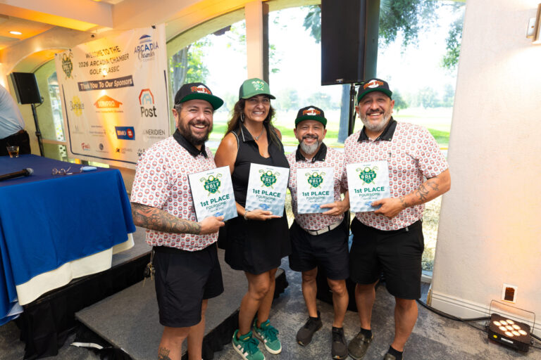a woman in black with three men in colorful golf shirts holding plaques