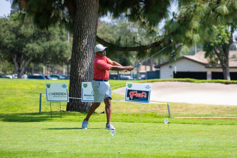 a man in a red shirt driving a ball on a golf course