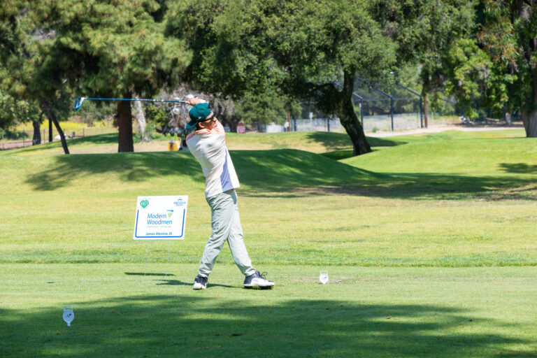 a man in a white shirt and gray pants drives a ball on a golf course