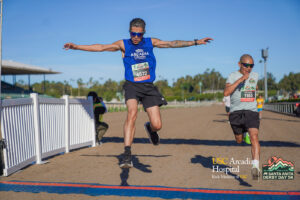 a man in a blue tank top jumping over the finish line at a race