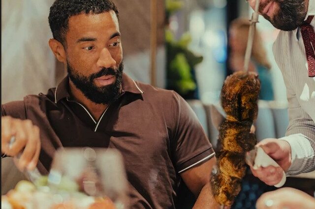 a man staring at a skewer of meats at Fogo de Chao