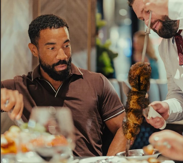 a man staring at a skewer of meats at Fogo de Chao